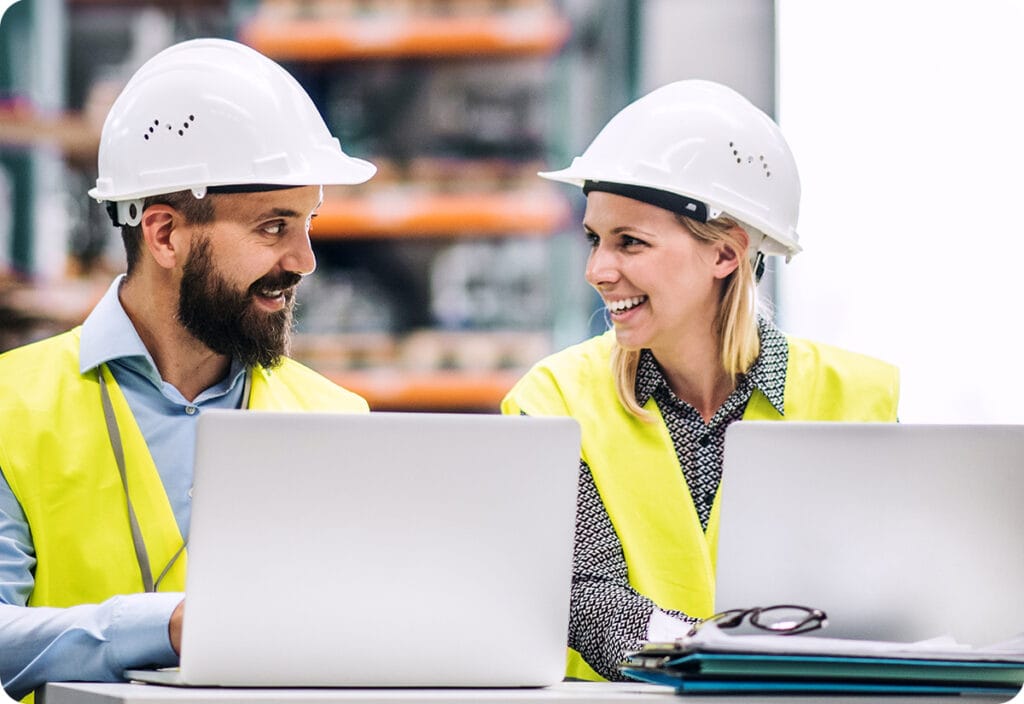 Warehouse employees both working on improving their transport management system software on laptops