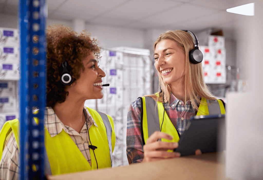 Two female employees reviewing logistics data on a tablet with white boxes, temperature controlled storage.