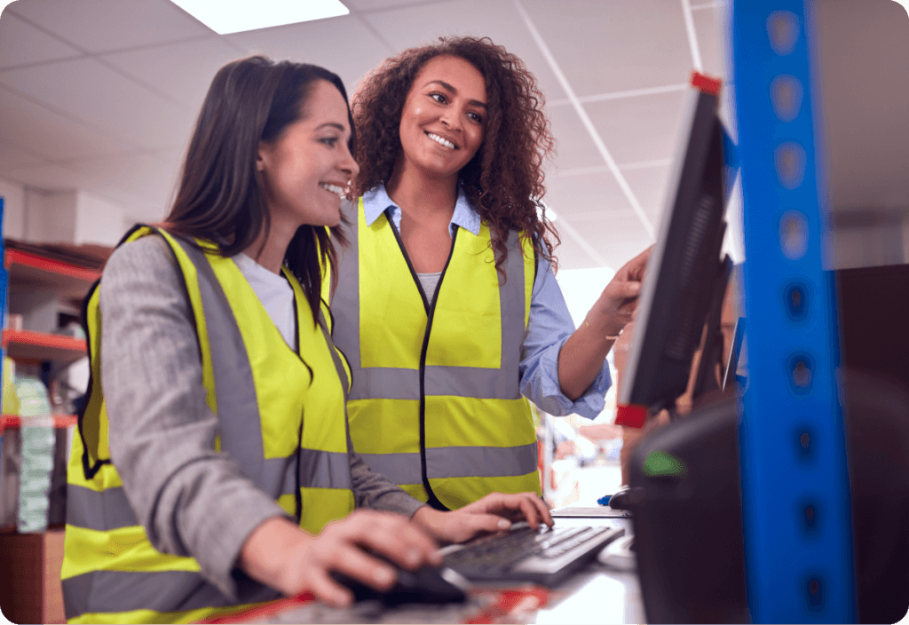 Two female employees reviewing freight invoice on computer monitor while one types on keyboard